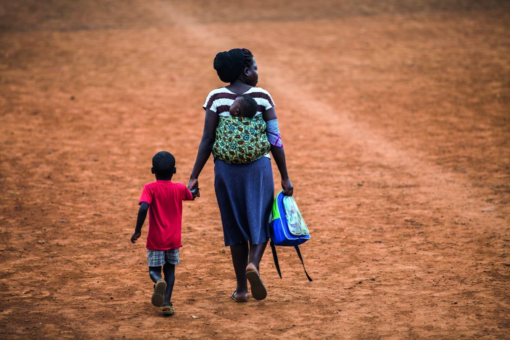 KAMPALA, UGANDA - CIRCA NOVEMBER 2016: An Ugandan mother with her baby on back, has taken her son from school and is going home.